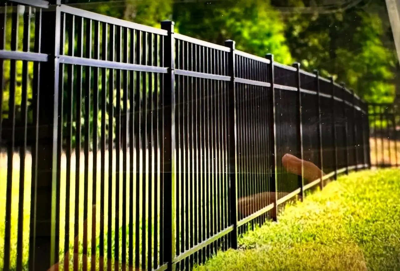 Black aluminum picket fence running along a green lawn