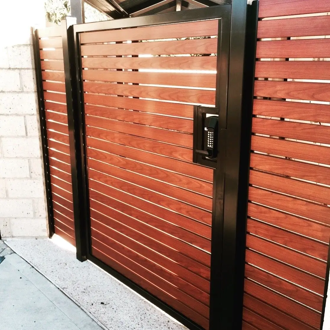 Horizontal wood-look slat gate in a black steel frame with keypad lock
