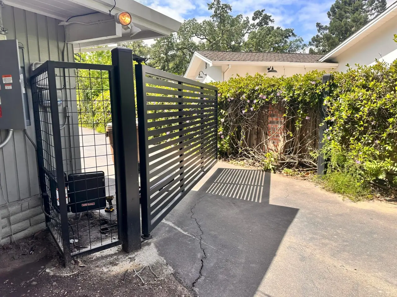 Modern black horizontal-slat swing gate with a LiftMaster operator in a protective cage