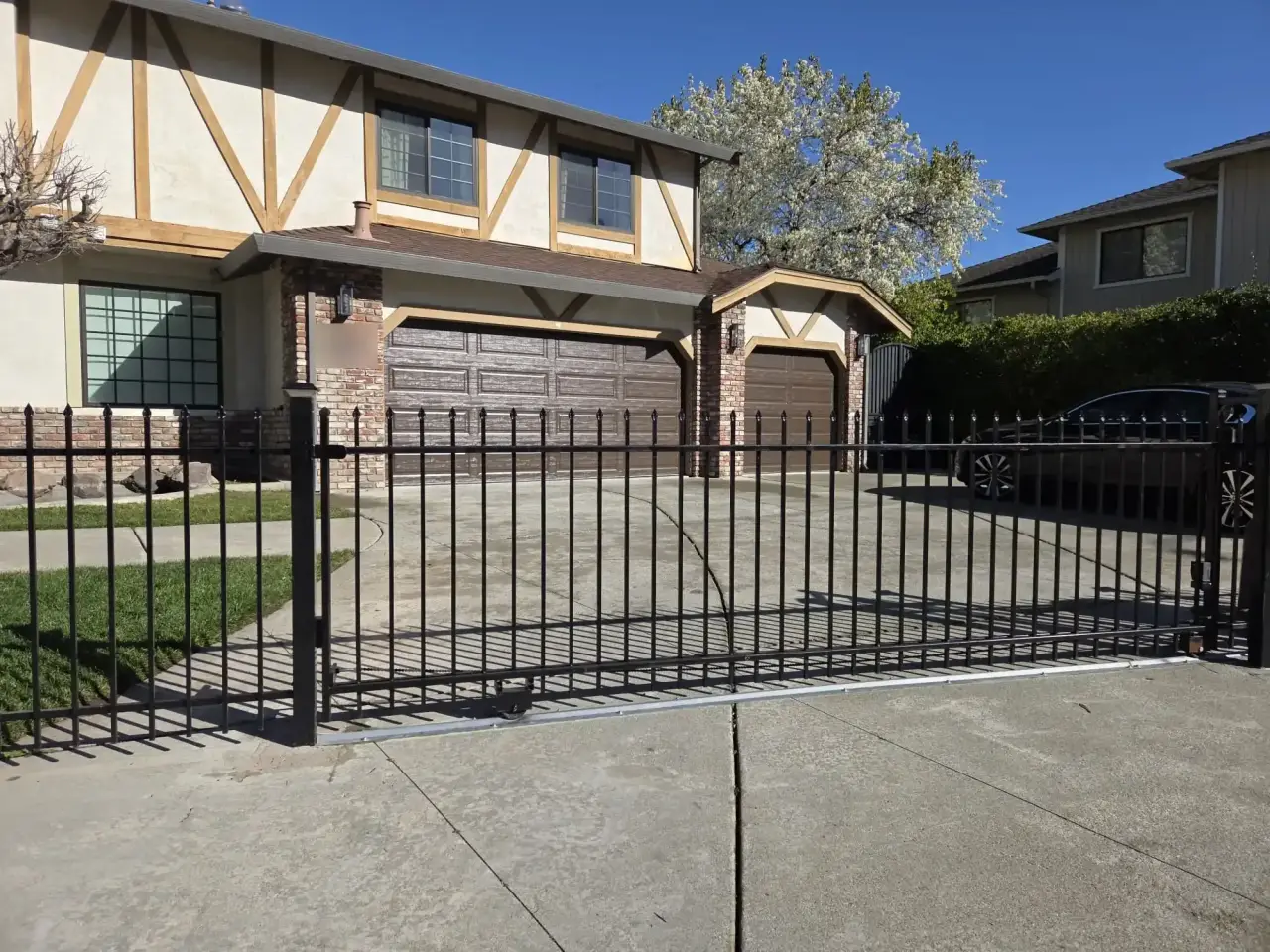 Black steel sliding driveway gate with spear-top pickets in front of a two-story home